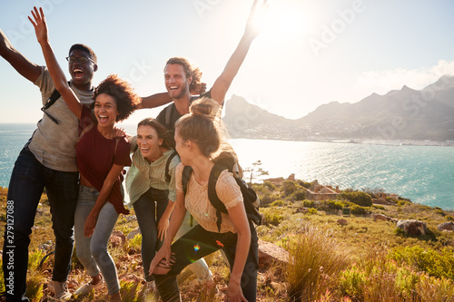Millennial friends on a hiking trip celebrate reaching the summit and have fun posing for photos