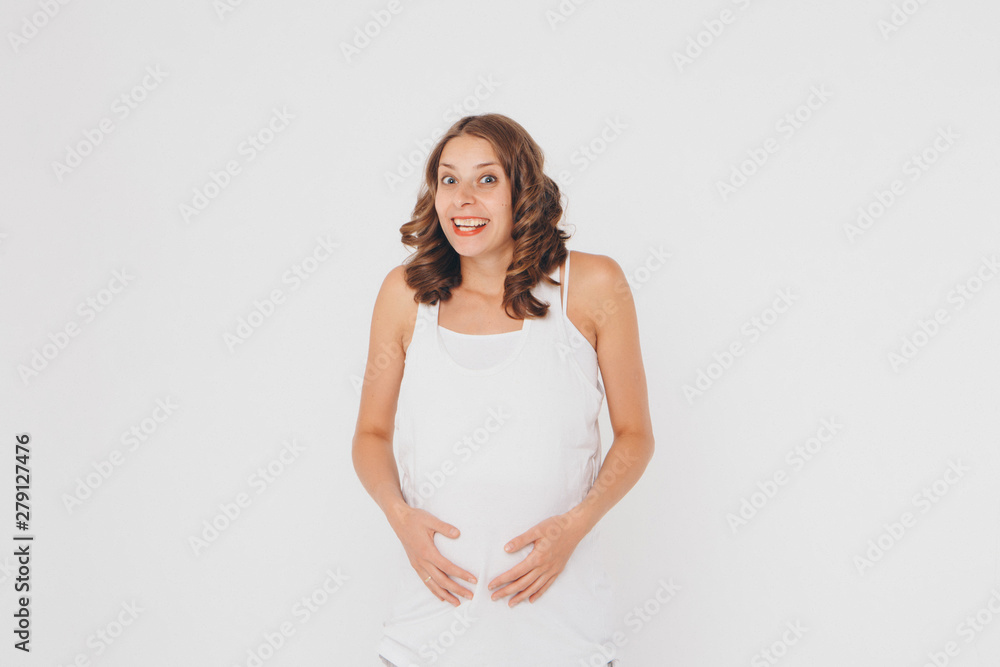 pregnant woman in sportswear on white background. The girl holds her stomach with her mouth wide open and a surprised expression on her face pregnant woman in sportswear on white background. The girl holds her stomach with her mouth wide open and a surprised expression on her face