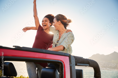 Two millennial female friends on a road trip standing in the back of an open top car, close up © Monkey Business