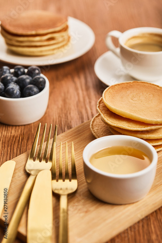 selective focus of bowl with honey  pancakes and blueberries near cup of coffee on wooden surface