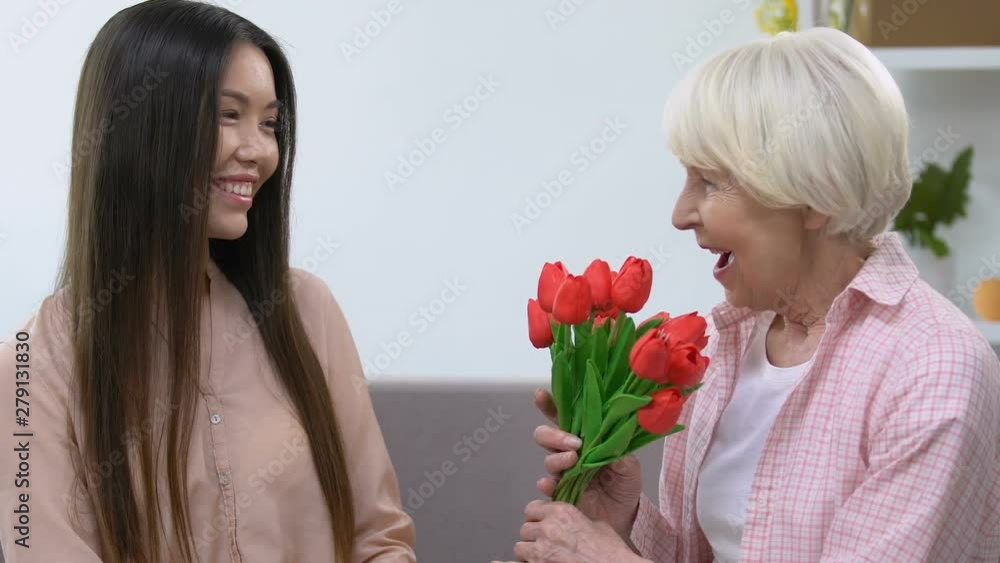 Granddaughter presenting grandmother bunch of tulips, holiday celebration Granddaughter presenting grandmother bunch of tulips, holiday celebration