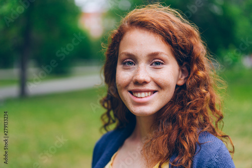Close-up portrait of beautiful young lady with long red hair and freckles smiling looking at camera in park in summer. Nature, people and happiness concept. photo
