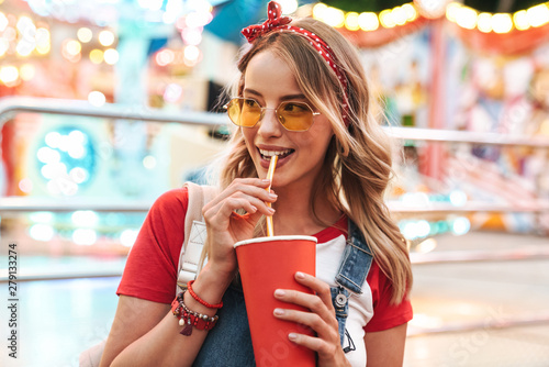 Image of attractive charming woman drinking soda beverage from paper cup while walking in amusement park