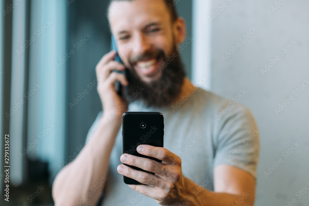 Business communication. Closeup of smartphone in man hand. Blurred bearded hipster guy busy with phone conversation, smiling. Business communication. Closeup of smartphone in man hand. Blurred bearded hipster guy busy with phone conversation, smiling.