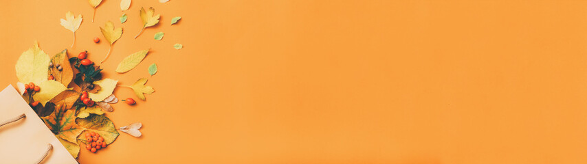 Fall season new collection. Cropped shot of yellow leaves scattered from shopping bag over orange background. Copy space.