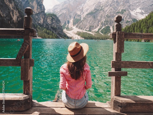 The girl with long hair wearing a wide-brimmed hat and a shirt striped on a background of Lake Lago di Braies in the Dolomites, South Tyrol, Italy. Pier with romantic old wooden rowing boats  © KseniaJoyg