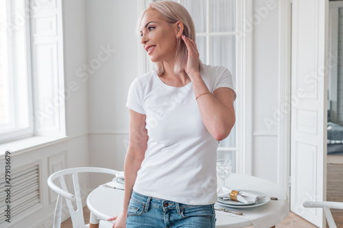 Promotional portrait of a happy blonde in a white t-shirt in the room
