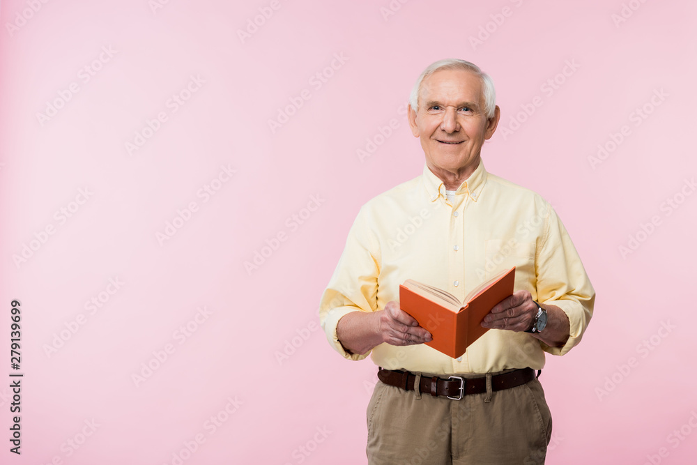 positive retired man holding book and smiling on pink positive retired man holding book and smiling on pink
