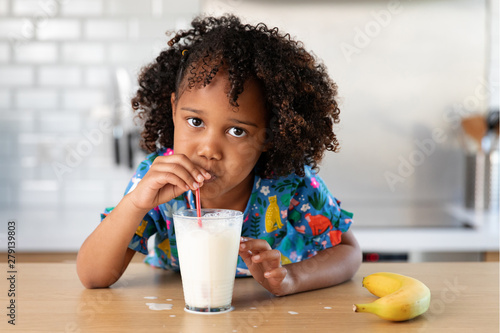 Young girl with afro hair blowing bubbles in a glass of milk