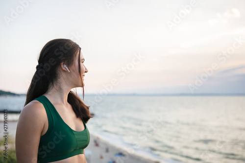 Pretty brunette woman resting after mornong jogging at the sea shore at sunrise listening to the music. photo