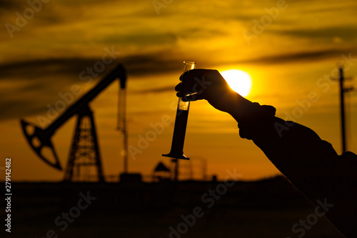 A man holding a flask of oil. Oil rigs in the background. Oil production in Russia. Sunset.