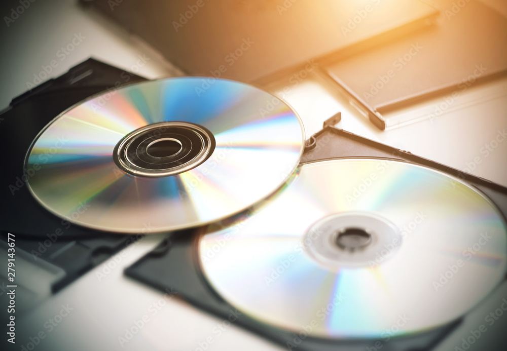 Two CDs for music, video and recording information, which are now less and less used out of use, lie on a white table, illuminated by sunlight. Two CDs for music, video and recording information, which are now less and less used out of use, lie on a white table, illuminated by sunlight.