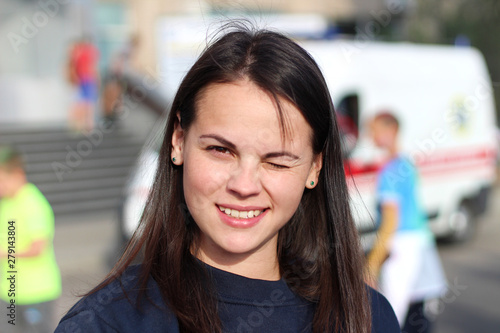 long-haired brunette girl smiling in the square on the background of an ambulance. Portrait of european woman in blue sweatshirt