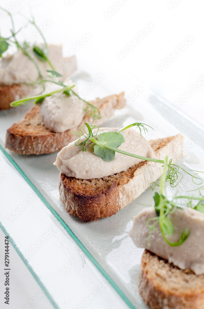 Bruschetta with liver pate and herbs on white table. Canape mini sandwiches Isolated on background. Banquet service with different food snacks and appetizers. Catering food, snacks. Party food. Bruschetta with liver pate and herbs on white table. Canape mini sandwiches Isolated on background. Banquet service with different food snacks and appetizers. Catering food, snacks. Party food.