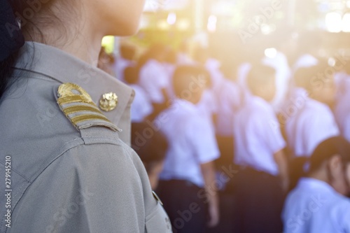 Female teachers wear Thai government uniforms behind the scenes as primary students are lining up.