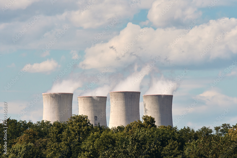 View of smoking chimneys of nuclear power plant, power lines and forest, under blue sky with clouds View of smoking chimneys of nuclear power plant, power lines and forest, under blue sky with clouds