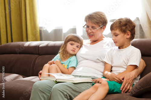 Grandmother with two child grandsons having a great time and reading a book at home. Family Reading Leisure 