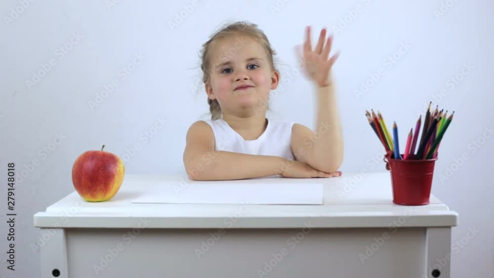 A cheerful little girl at her desk pulls in her hand and laughs. Portrait of a little schoolgirl A cheerful little girl at her desk pulls in her hand and laughs. Portrait of a little schoolgirl
