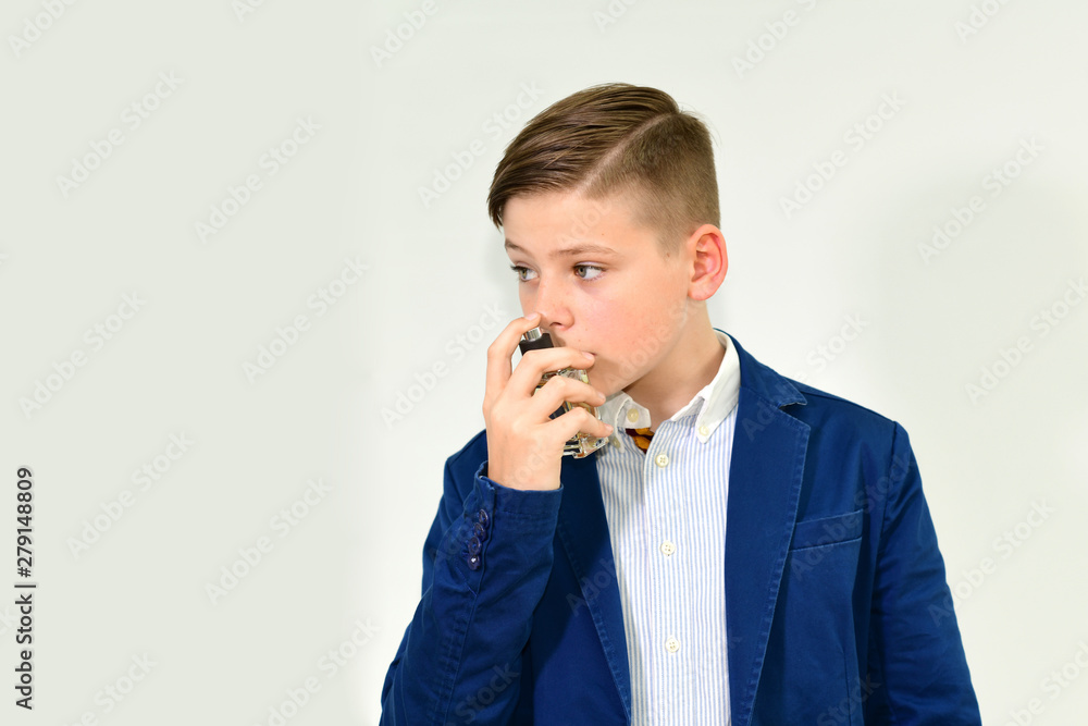 Picture of young handsome boy in blue jacket smelling perfume grey  background. Demonstration of Perfumes or ode colon, Eau de toilette. Copy  space, empty space for advertising for cosmetics. Stock Photo