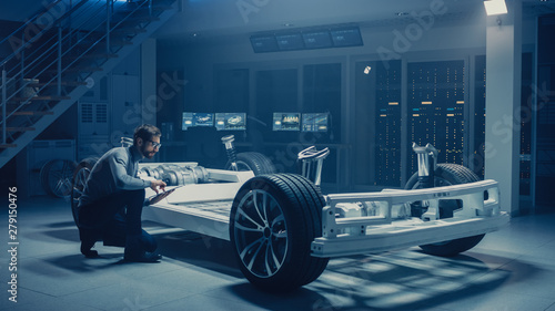 Automobile Engineer Working on Electric Car Platform Chassis Prototype, Using Tablet Computer with 3D CAD Software Modelling. Innovative Facility: Vehicle Frame with Wheels,Battery and Suspension