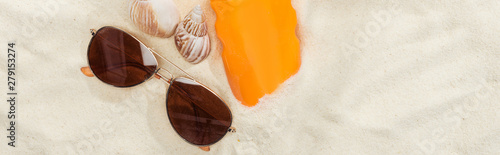 orange bottle of sunscreen on sand near seashells and sunglasses, panoramic shot