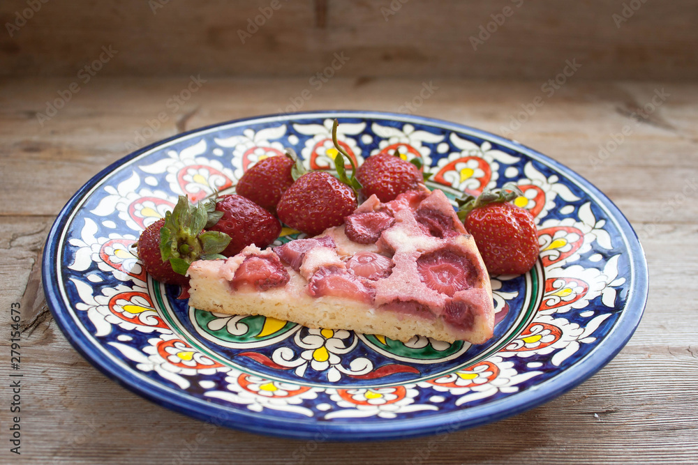 Piece of round strawberry berries tart pie pudding on plate with blue pattern on rustic wooden background Piece of round strawberry berries tart pie pudding on plate with blue pattern on rustic wooden background