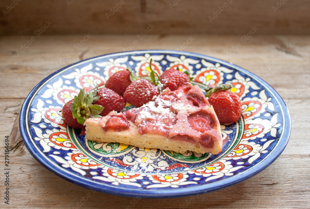 Piece of round strawberry berries tart pie pudding on plate with blue pattern on rustic wooden background