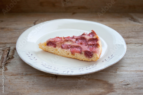 Piece of round strawberry berries tart pie pudding on white plate on rustic wooden background