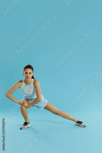 Fitness. Woman in sportswear stretching legs on blue background