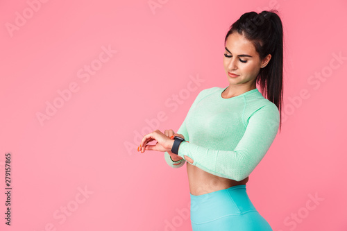 Pretty young sports fitness woman isolated over pink wall background using watch clock.