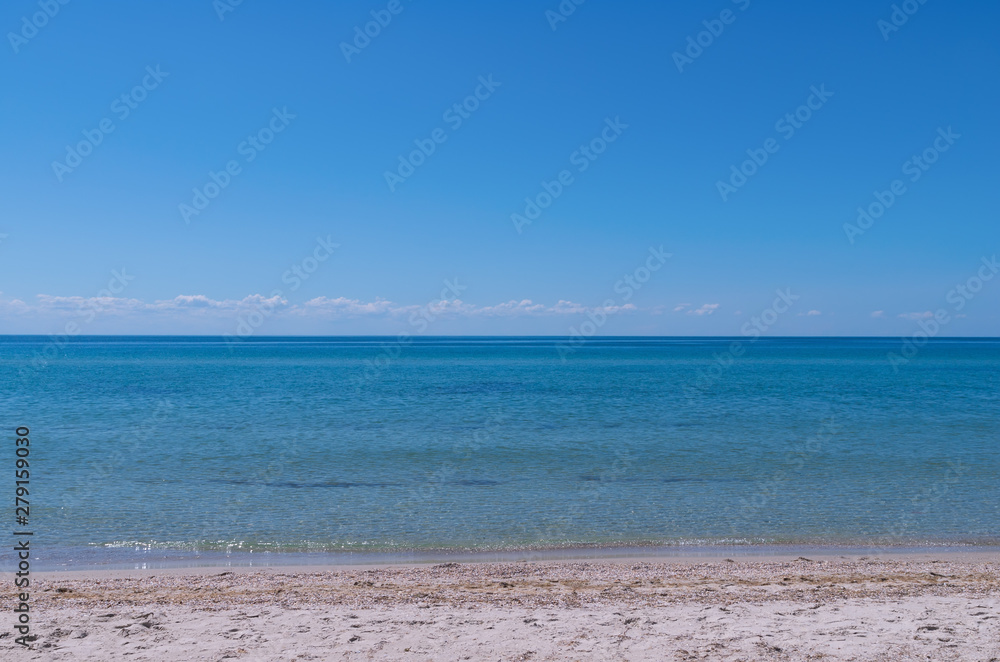 Beautiful blue colors of the ocean, sea and sky, copy space for text or the design background. Sea waves with shine on sandy beach, row of small white clouds above the horizon. Summer vacation or rest