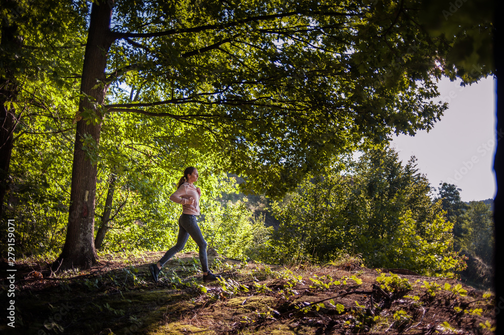 Young girl jogging in the woods on a sunny morning.
