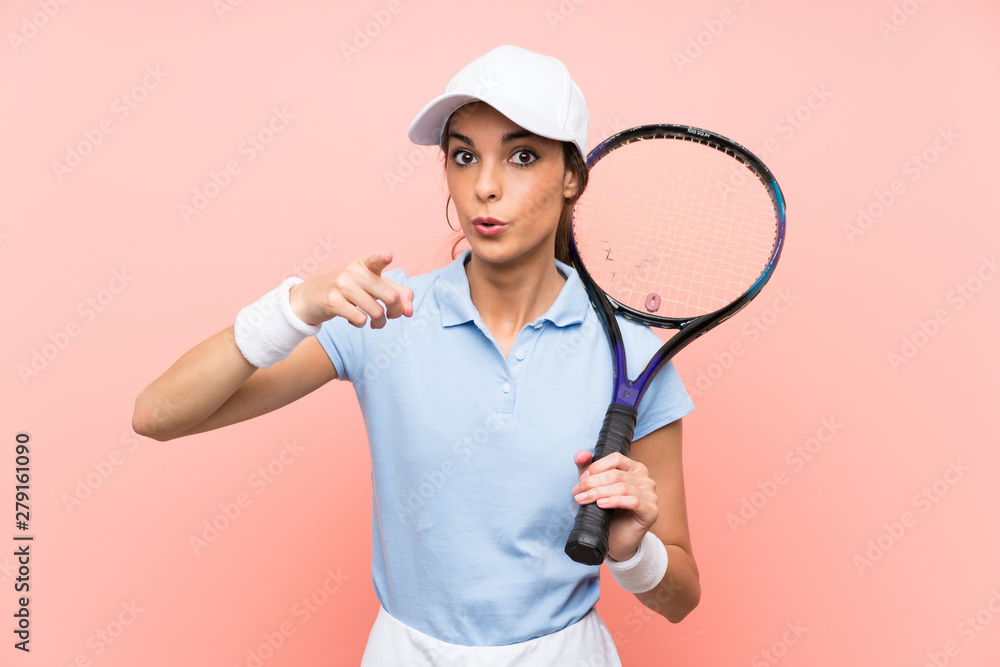 Young tennis player woman over isolated pink wall surprised and pointing front