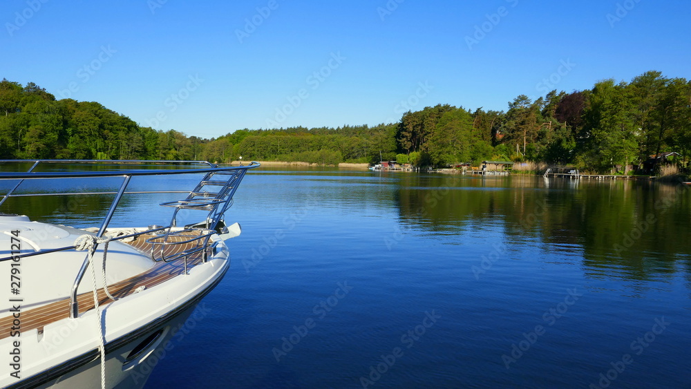 weißes Boot fährt auf stillem See umrahmt von grünem Wald in der Mecklenburger Seenplatte