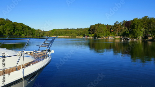 weißes Boot fährt auf stillem See umrahmt von grünem Wald in der Mecklenburger Seenplatte
