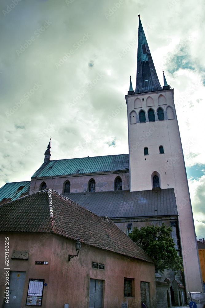 Tower Oleviste with old extensions in the old city of Tallinn with clouds in the sky. The roof is green copper. Clouds in the sky. Bottom view with perspective. Tinted in yellow.