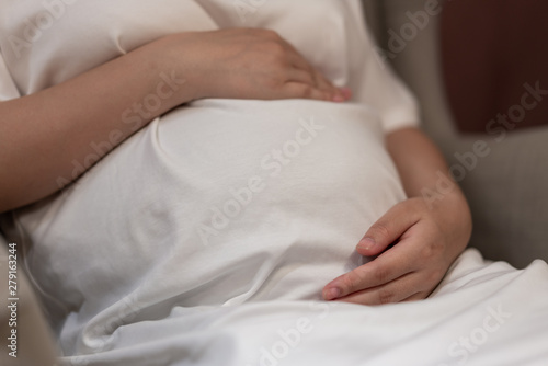 Young pregnant woman holds her hands on her swollen belly