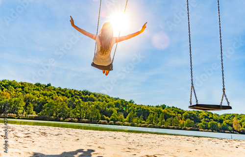 Frau auf einer Schaukel an einem See mit Sandstrand