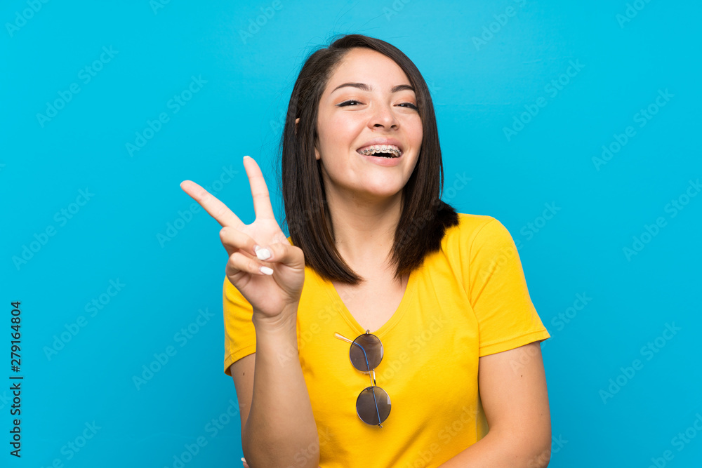 Young Mexican woman over isolated blue background smiling and showing victory sign Young Mexican woman over isolated blue background smiling and showing victory sign