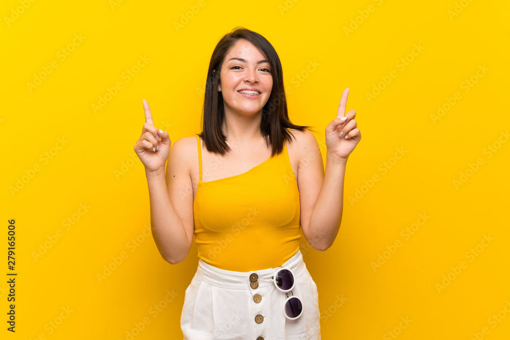 Young Mexican woman over isolated yellow background pointing up a great idea Young Mexican woman over isolated yellow background pointing up a great idea