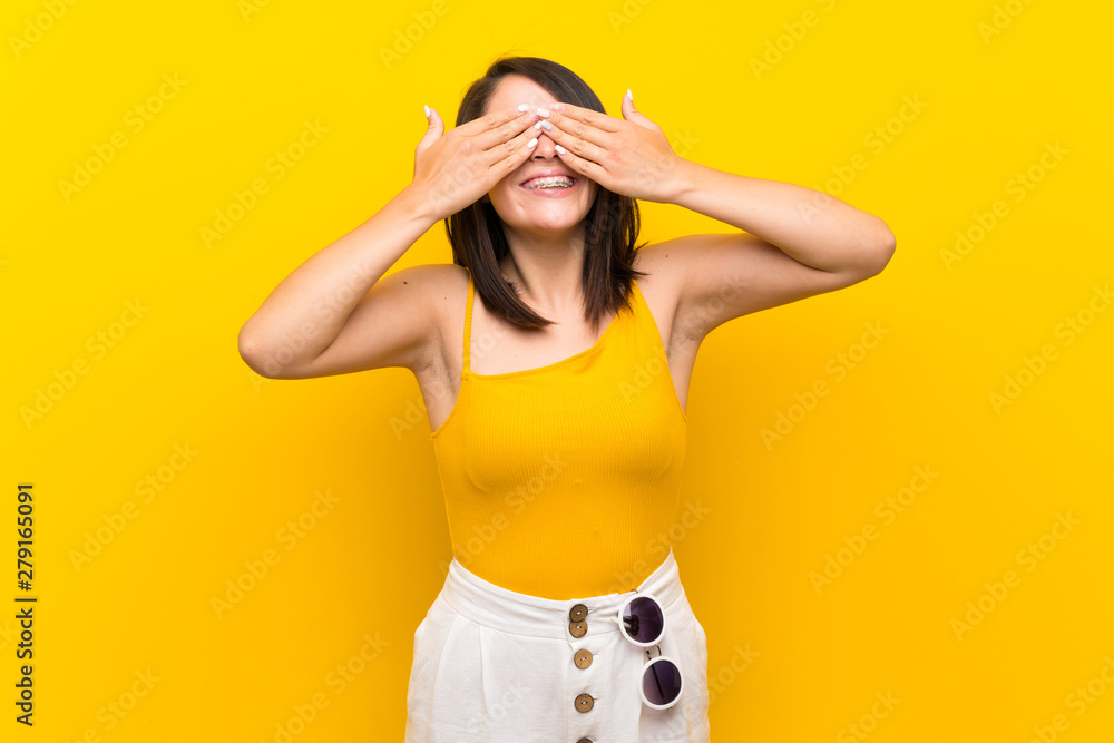 Young Mexican woman over isolated yellow background covering eyes by hands Young Mexican woman over isolated yellow background covering eyes by hands