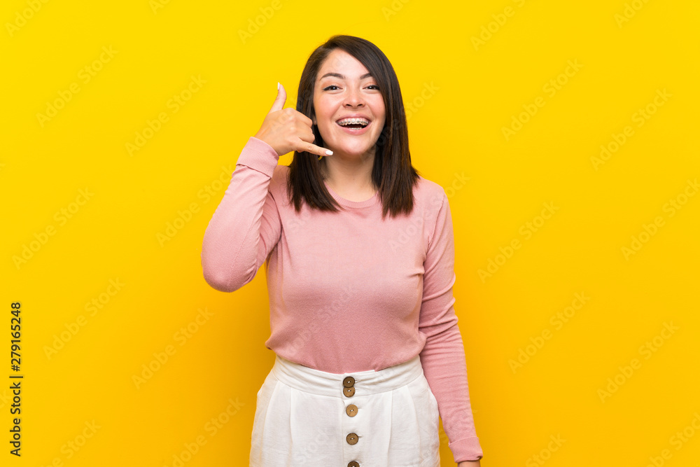 Young Mexican woman over isolated yellow background making phone gesture. Call me back sign Young Mexican woman over isolated yellow background making phone gesture. Call me back sign