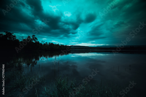 Fototapeta Naklejka Na Ścianę i Meble -  moonlight shines behind a cloudy at night over tranquil lake
