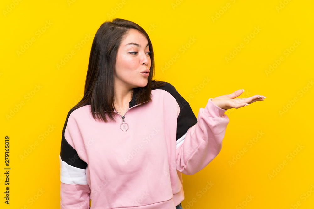 Young Mexican woman over isolated yellow background holding copyspace imaginary on the palm Young Mexican woman over isolated yellow background holding copyspace imaginary on the palm