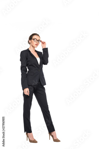full length view of young successful businesswoman in black suit and glasses isolated on white