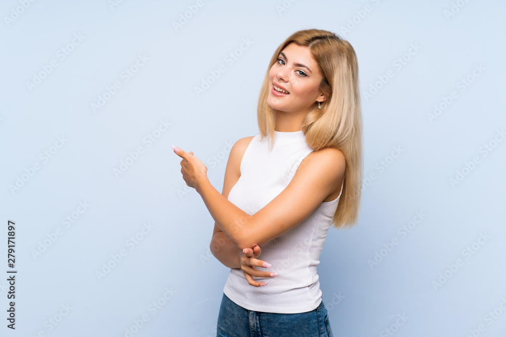 Teenager girl over isolated blue background presenting an idea while looking smiling towards Teenager girl over isolated blue background presenting an idea while looking smiling towards