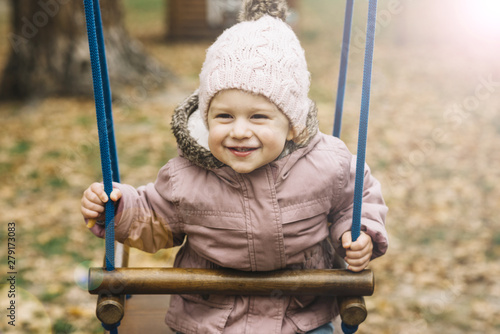 Sunlit little girl in warm clothes on swing © Freepik