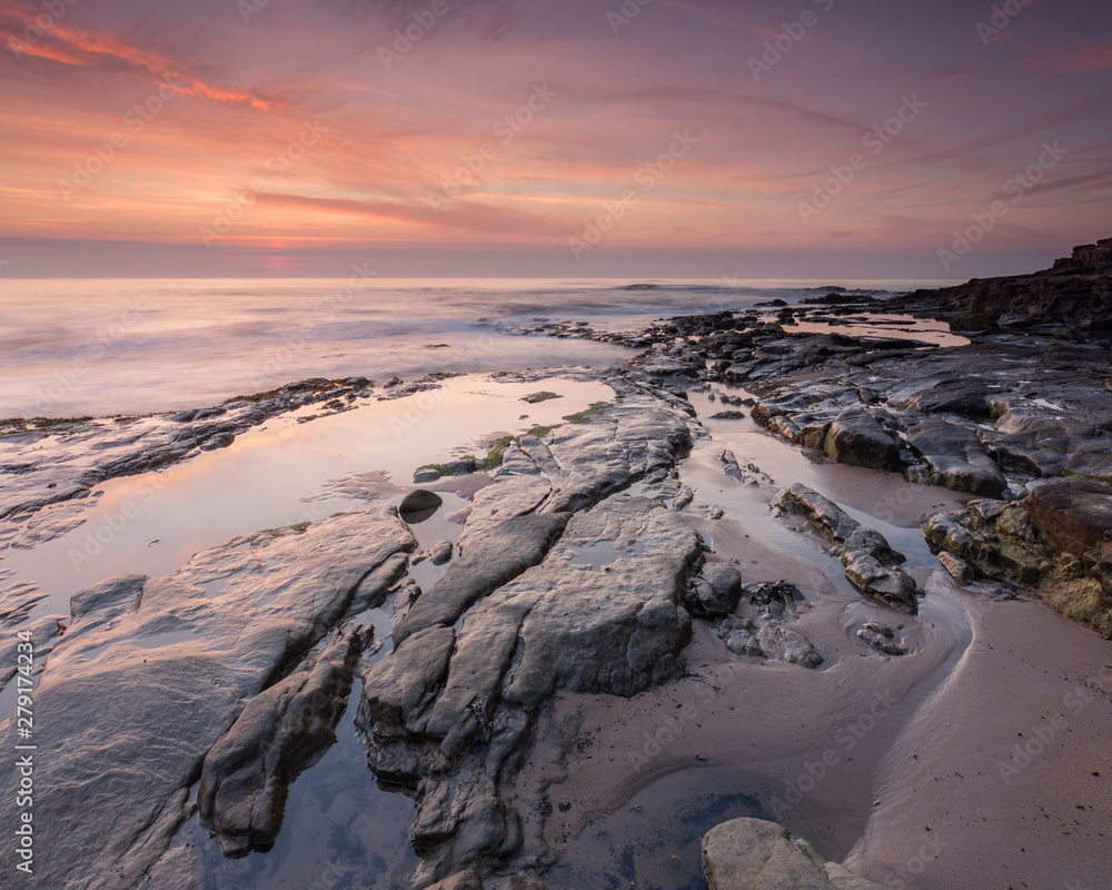 Obraz premium Sunrise and dawn light over the rocks on Cresswell Beach on the coast of Northumberland, England, UK.