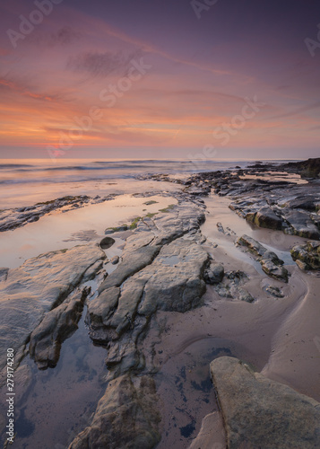 Sunrise and dawn light over the rocks on Cresswell Beach on the coast of Northumberland, England, UK.