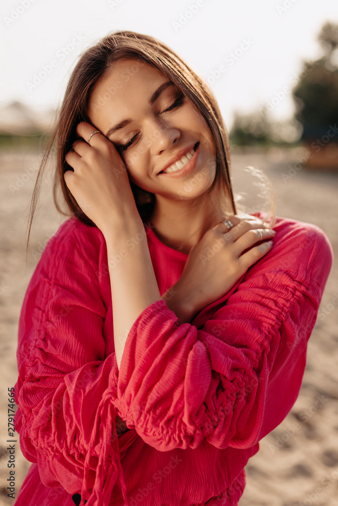 Close up Portrait of magnificent female model in pink blouse closed eyes and touching face with gentle smile